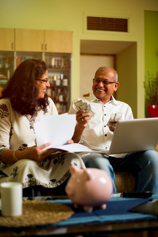 [freepicdownloader.com]-senior-indian-asian-couple-accounting-doing-home-finance-checking-bills-with-laptop-calculator-money-also-with-piggy-bank-while-sitting-sofa-couch-table-home-medium.jpg